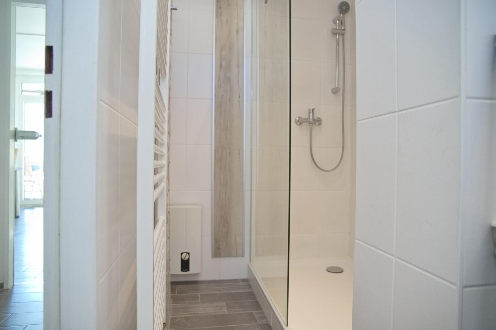 Dusche mit Glaswand, weißen Fliesen und Handdusche