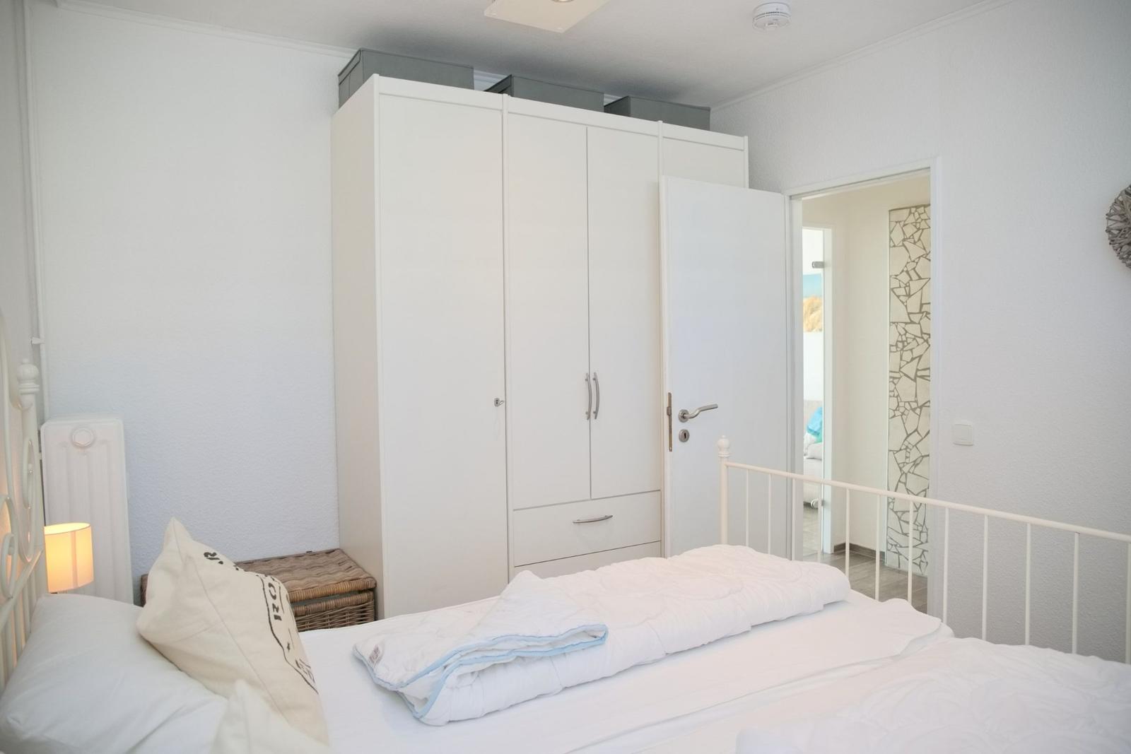Schlafzimmer mit weißem Bett, Kleiderschrank und Lampe.