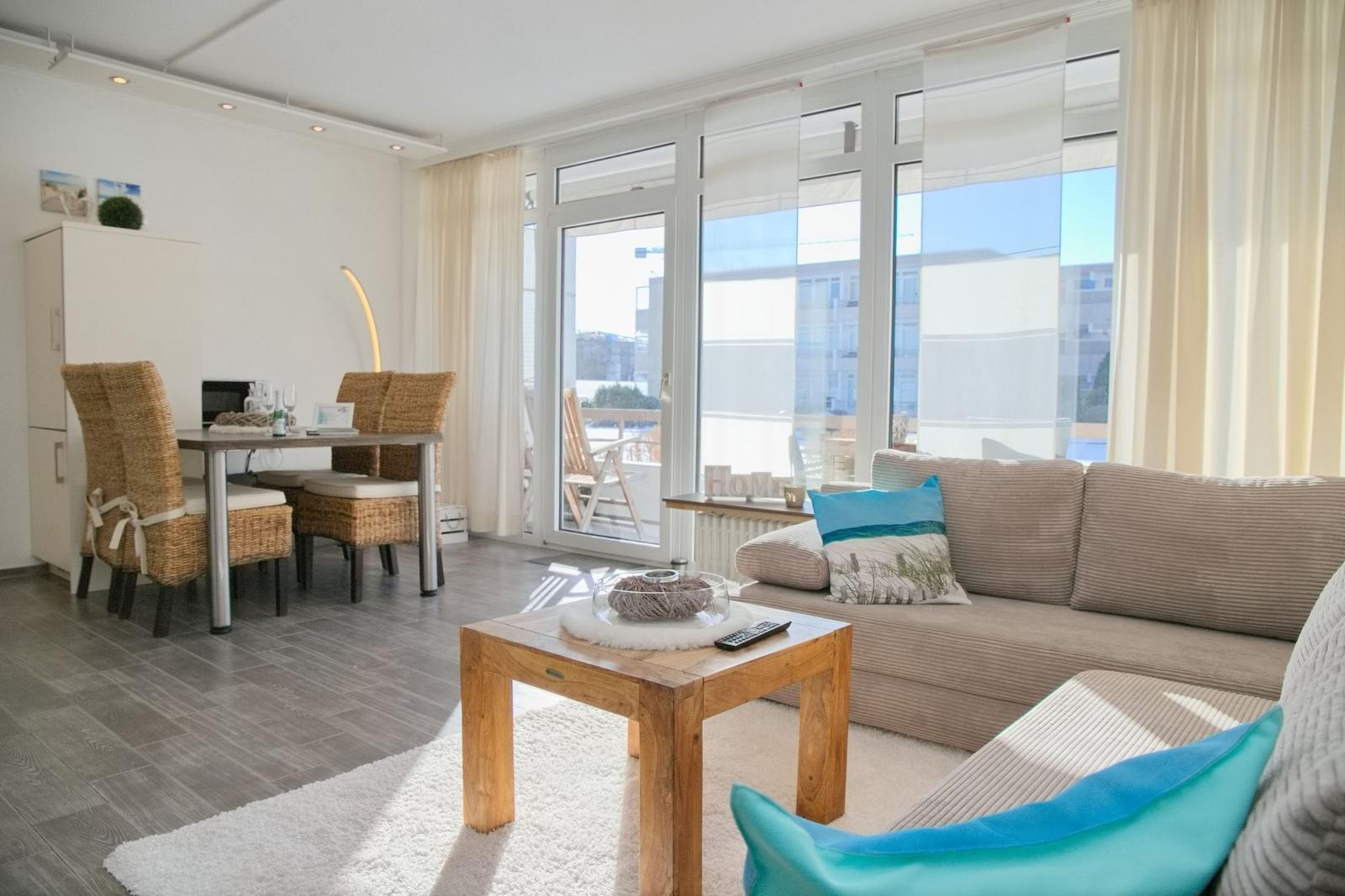 Wohn- und Essbereich mit Sofa, Tisch und Blick auf Balkon.