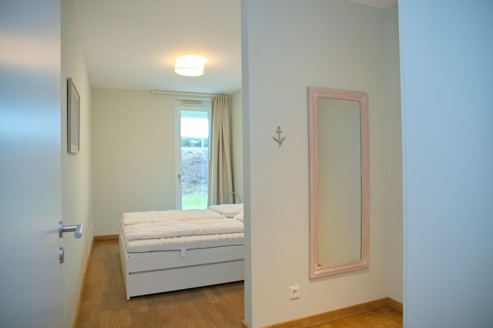 Schlafzimmer mit weißem Bett, Spiegel und Fenster zum Garten.