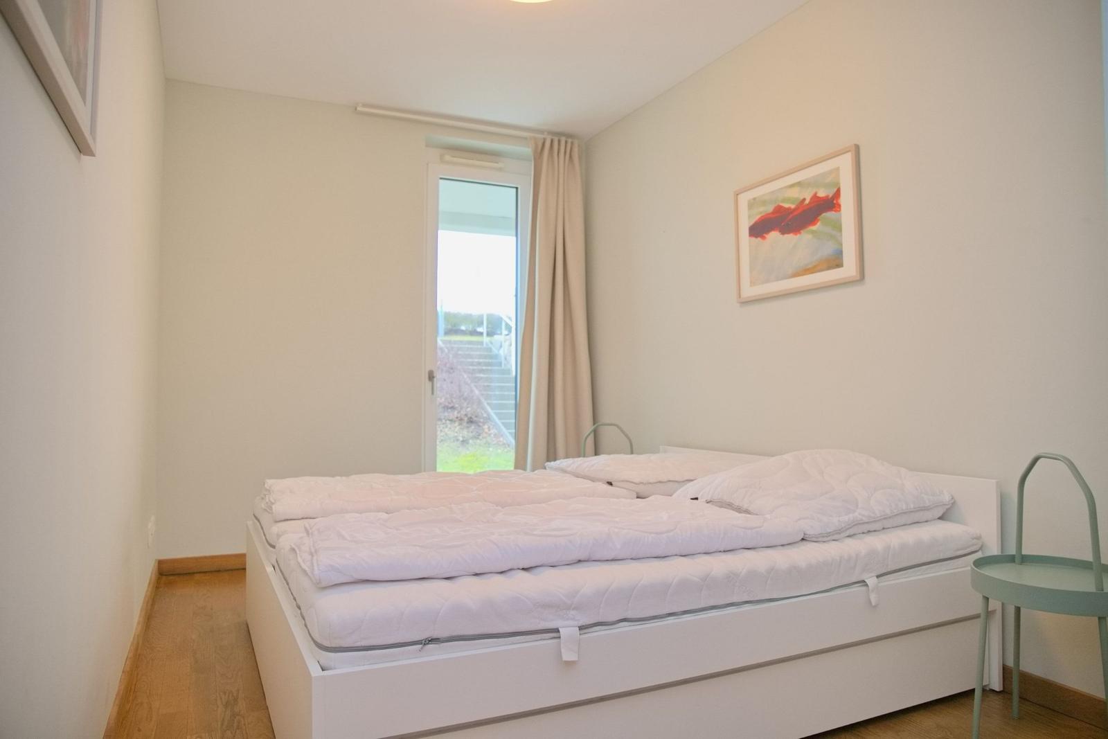 Schlafzimmer mit weißem Bett, Fenster und Bild an der Wand.