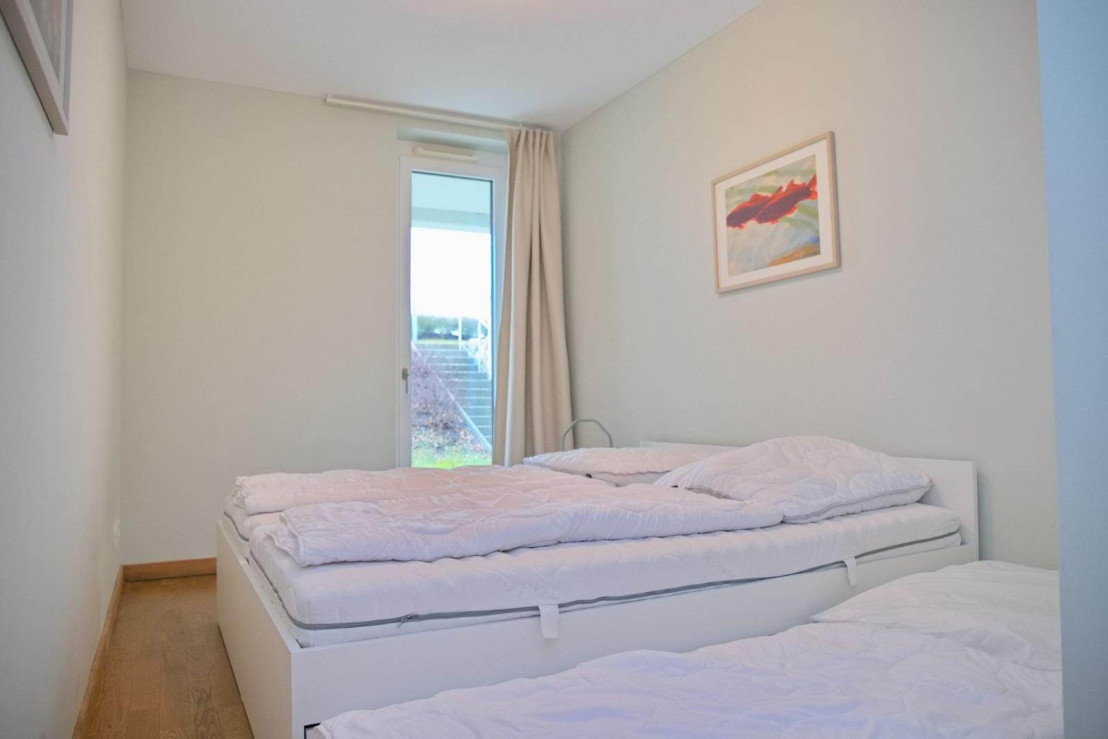 Schlafzimmer mit zwei Betten, Fenster und Wandbild.