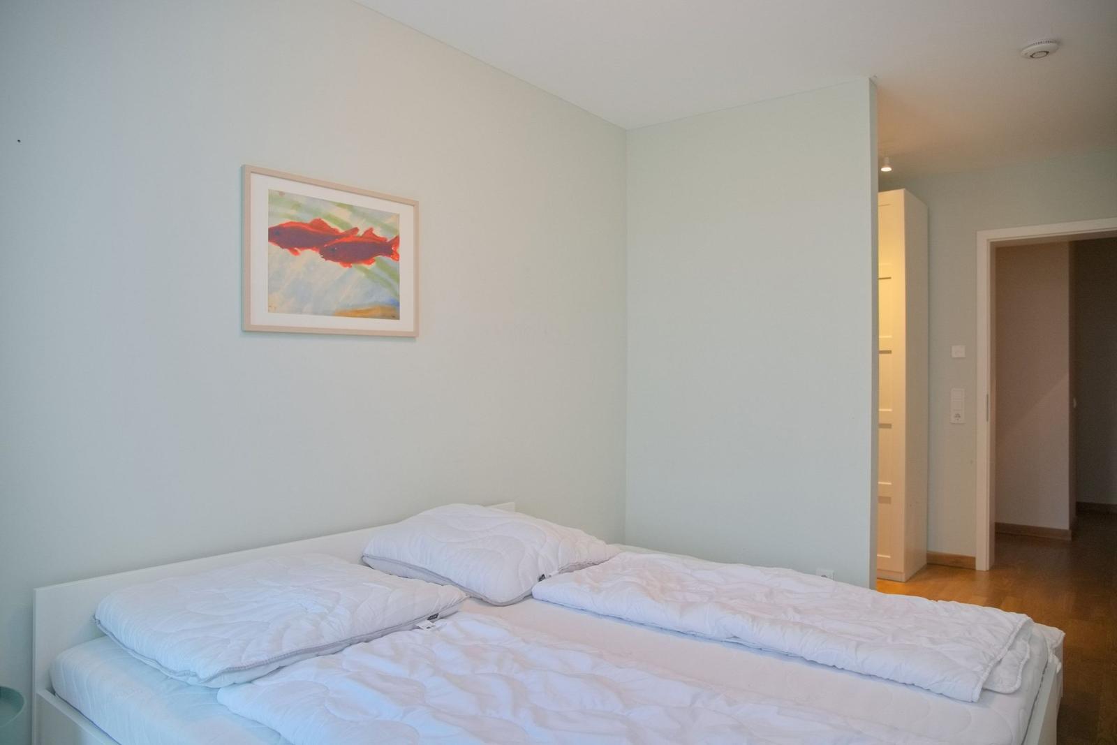 Schlafzimmer mit Bett, Wandbild und Blick in einen Flur.