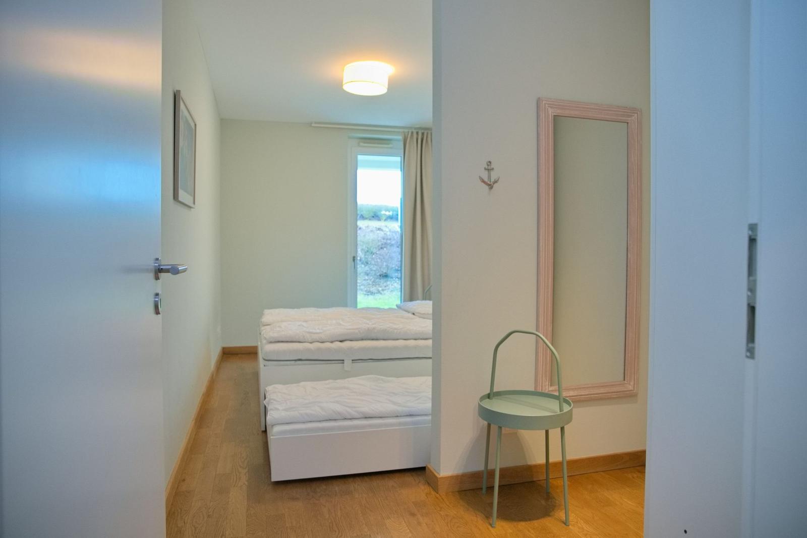 Schlafzimmer mit Bett, Spiegel und Stuhl. Tür führt ins Zimmer.
