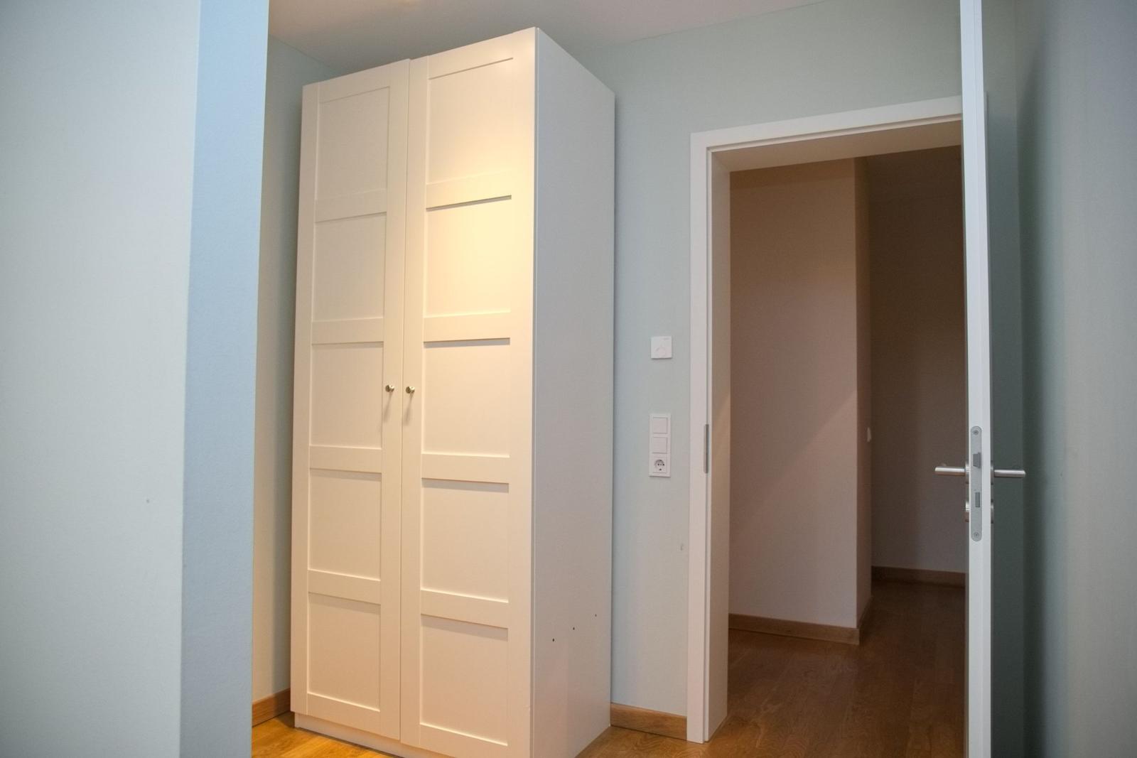 Schlafzimmer mit weißen Schrank und offener Tür zum Flur.