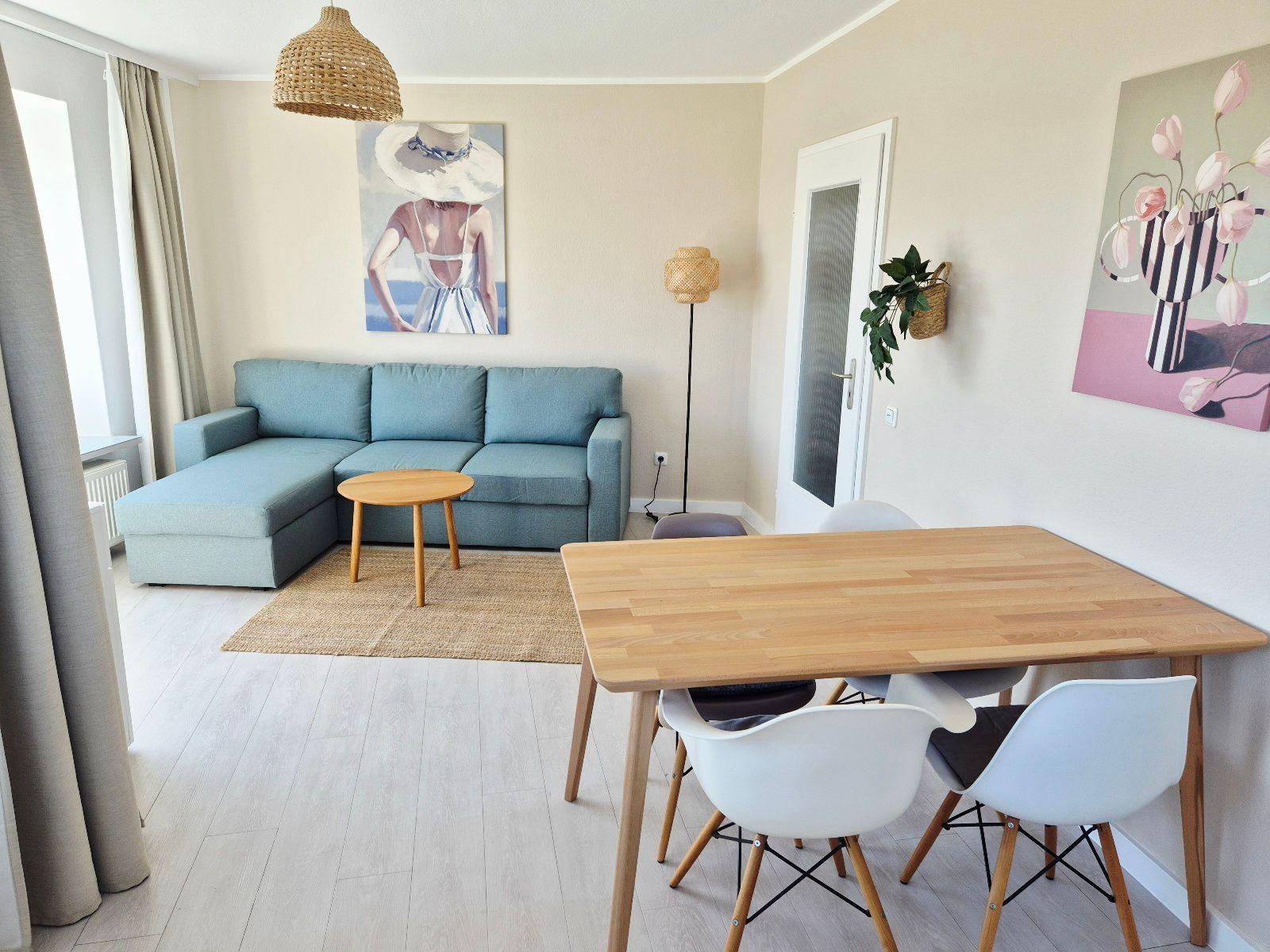 Wohn- und Essbereich mit Sofa, Tisch und Stühlen. Wandbilder und Pflanzen.