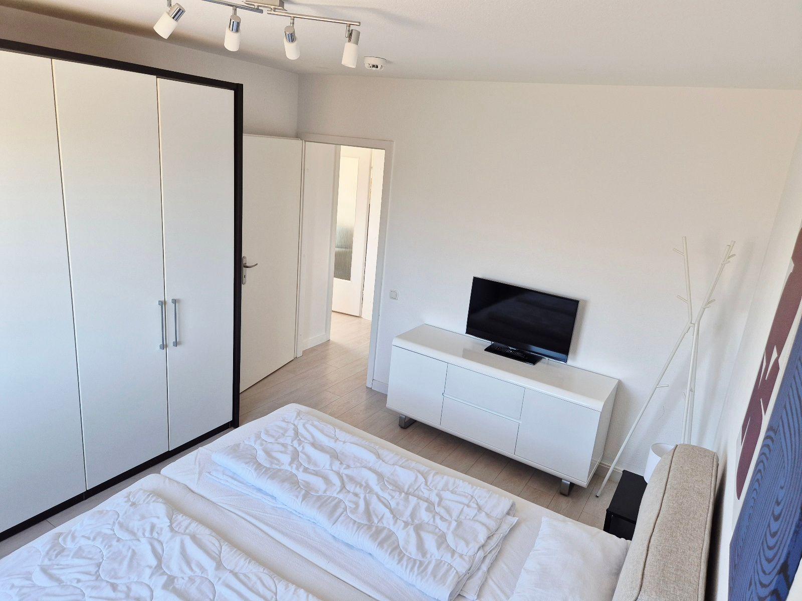 Schlafzimmer mit Bett, Kleiderschrank, TV und Stehlampe.