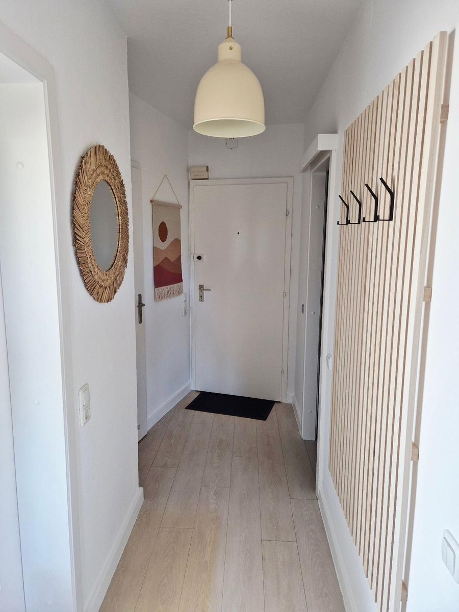Hausgang mit Holzboden, Wandspiegel und Garderobenwand mit Haken.