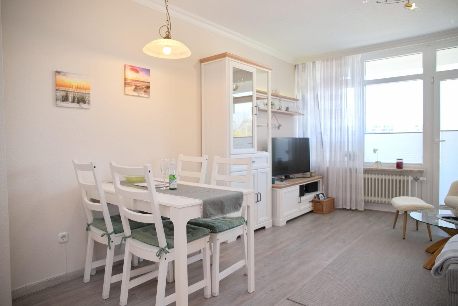 Esszimmer mit Tisch, Stühlen und Fernseher. Fenster mit Vorhängen und Bodenbelag.