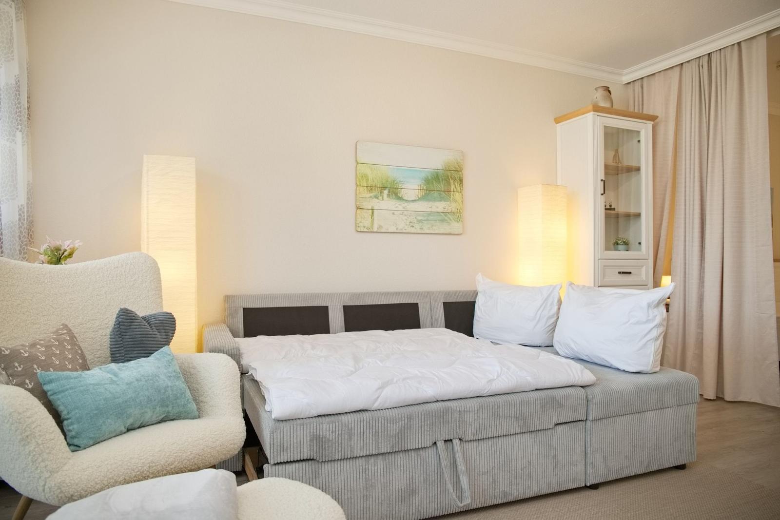 Schlafzimmer mit Bett, Sessel und Schrank. Wandbild und Stehlampen sorgen für Beleuchtung.