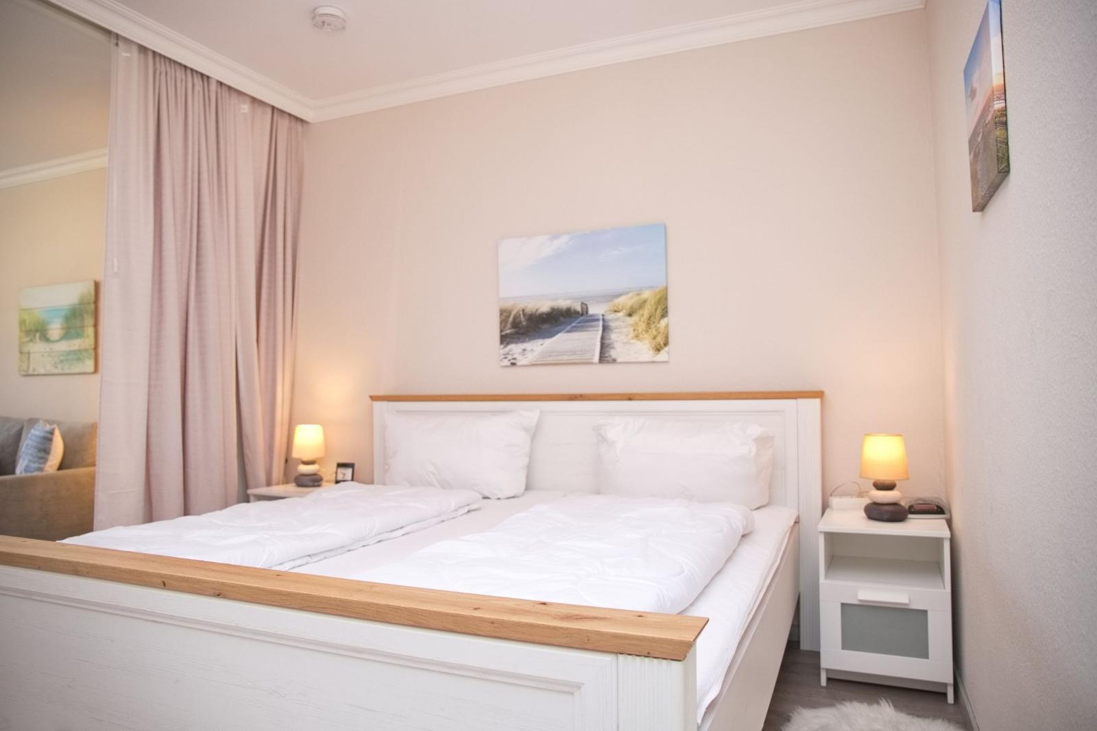 Schlafzimmer mit Doppelbett, Nachttischen und Wandbildern.