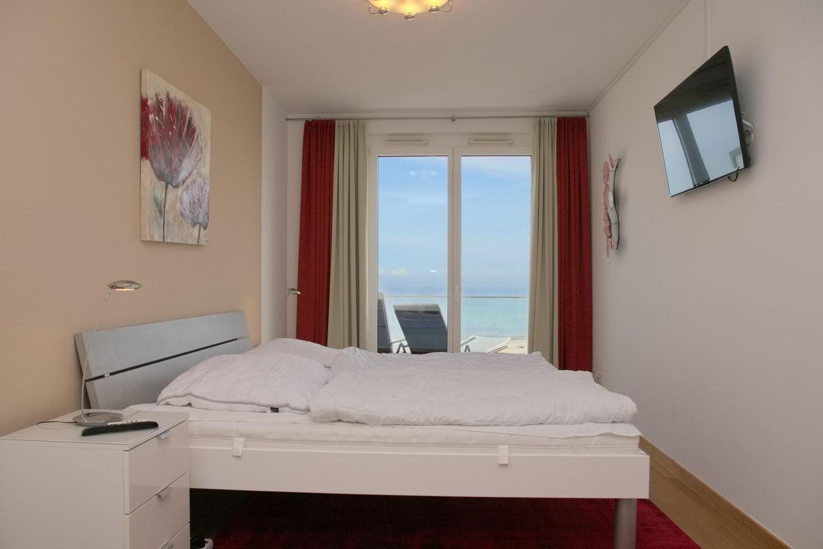 Schlafzimmer mit Bett, Fernseher und Meerblick durch Fenster.