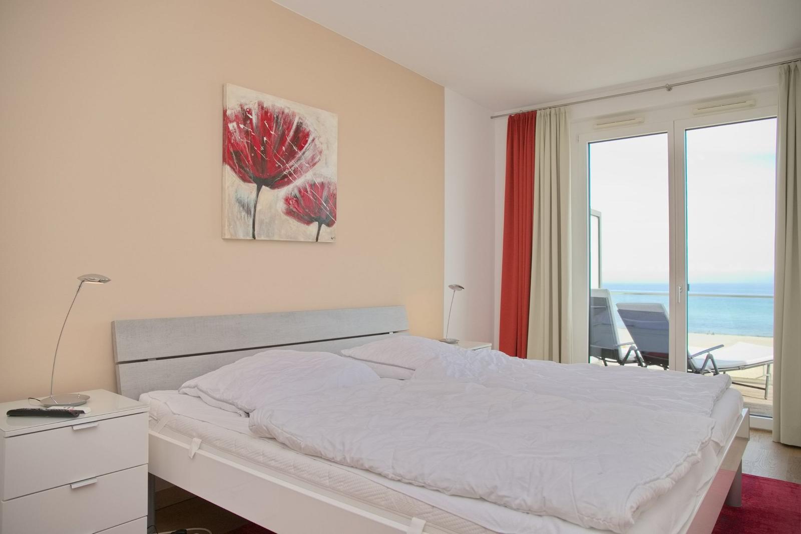 Schlafzimmer mit Bett, Nachttisch und Blick aufs Meer.