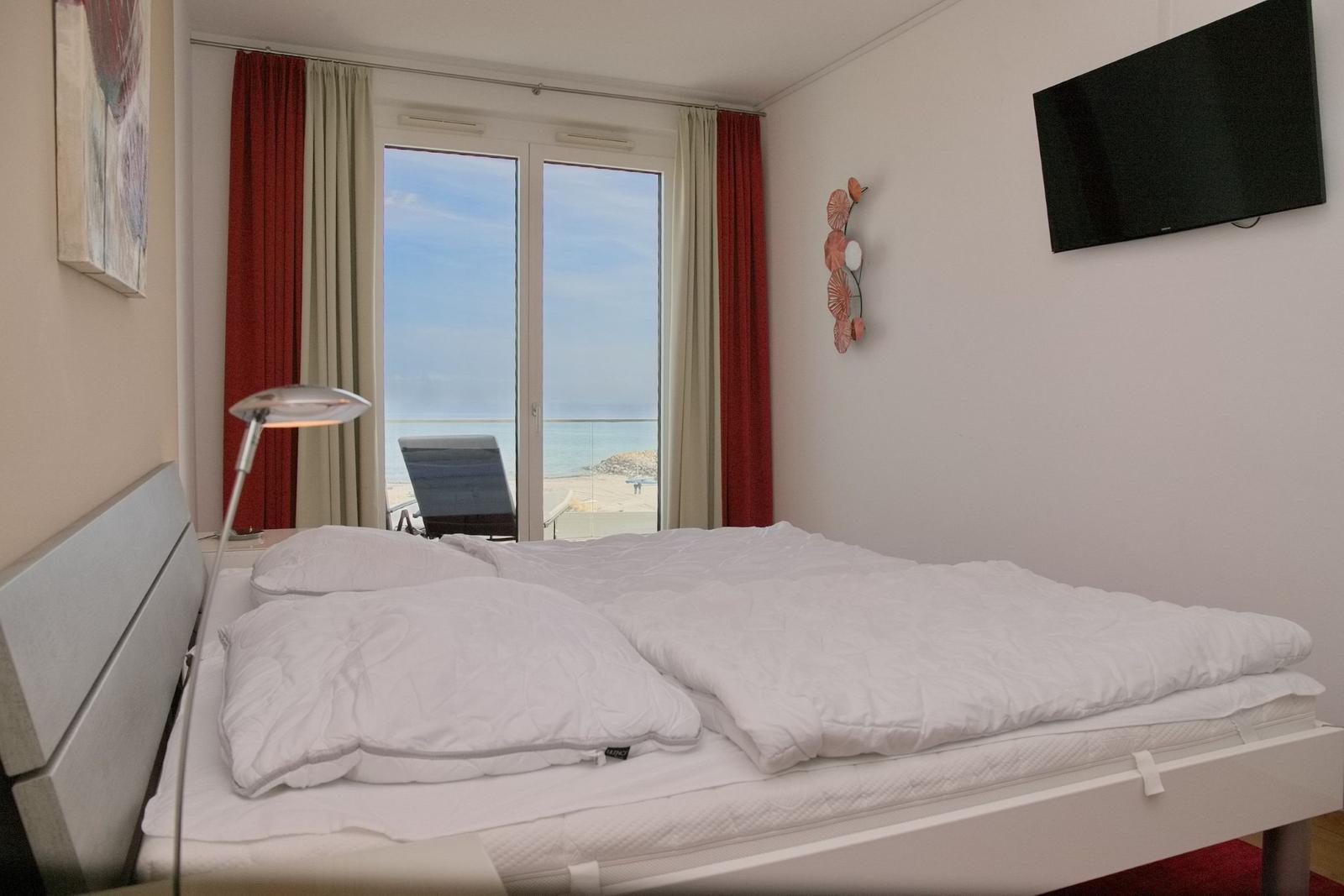 Schlafzimmer mit Blick aufs Meer, Bett, TV und Fenster mit Blick auf Strand.