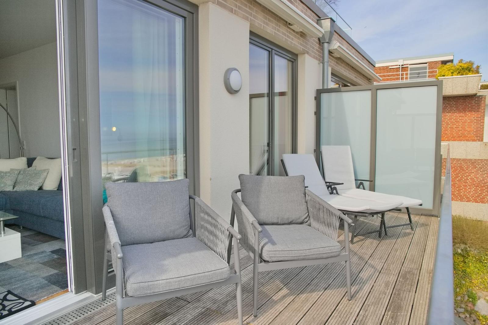 Terrasse mit zwei Sesseln und Liegen. Durchgehendes Glas führt ins Wohnzimmer.