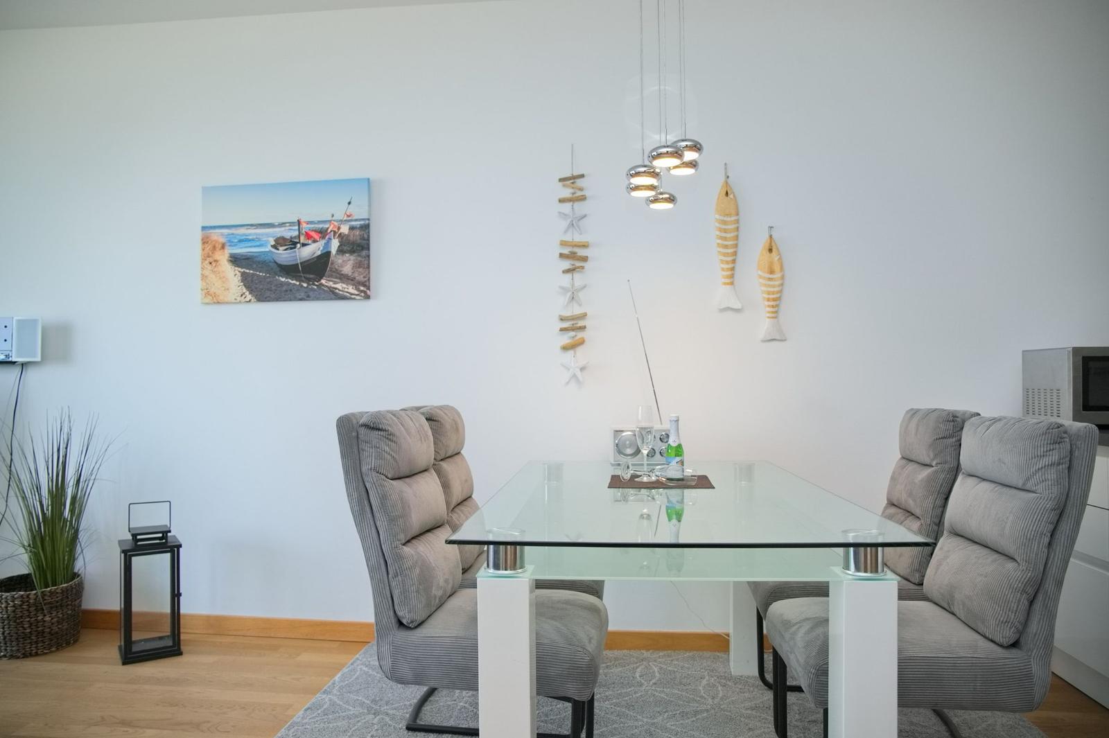 Esszimmer mit Glas-Tisch, grauen Stühlen und Wanddekoration mit Fischen.