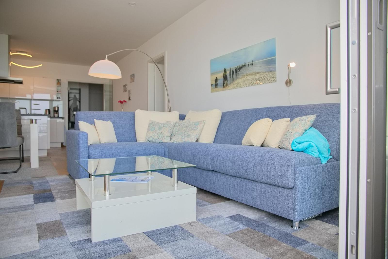 Ein Wohnzimmer mit blauem Sofa, Glas-Tisch und Wandbild.
