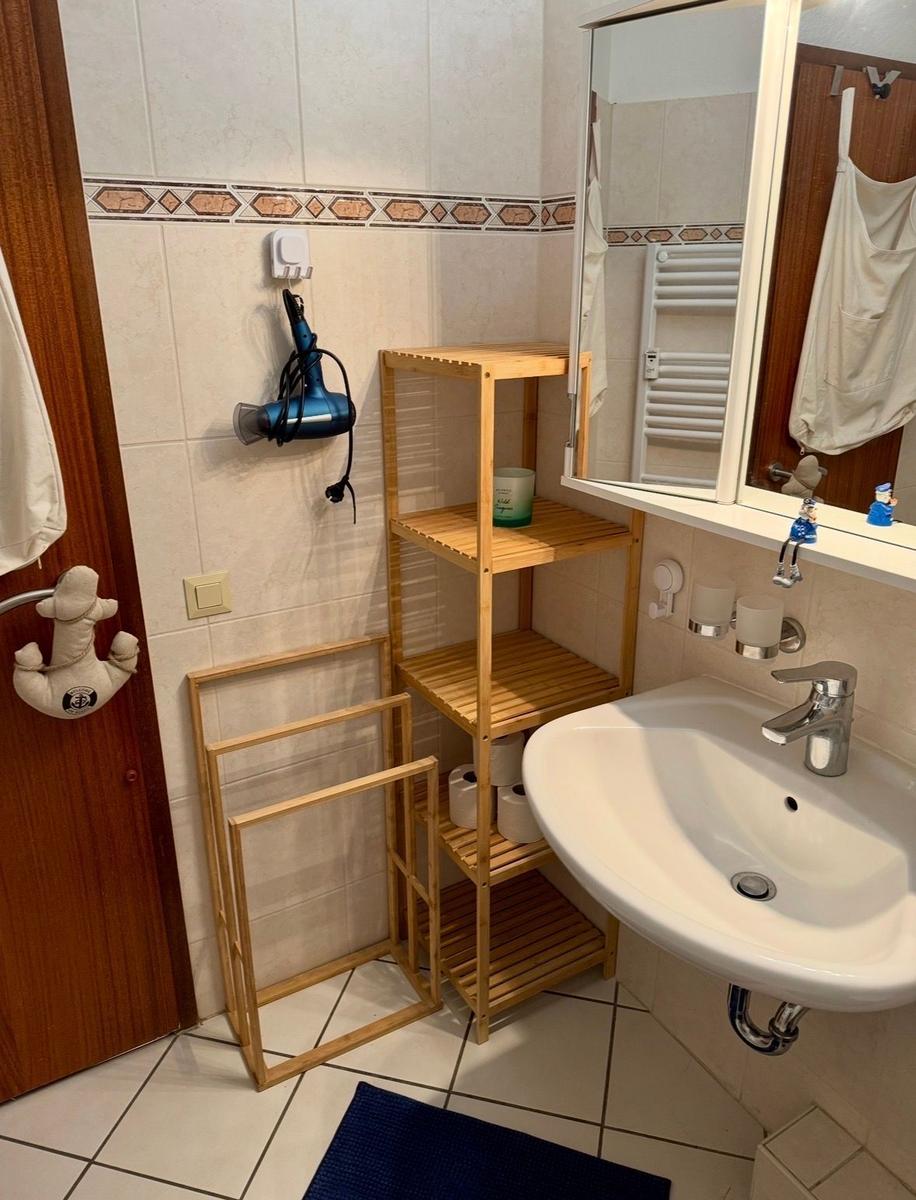 Badezimmer mit Waschbecken, Spiegel, Holzregal und Handtuchhalter.