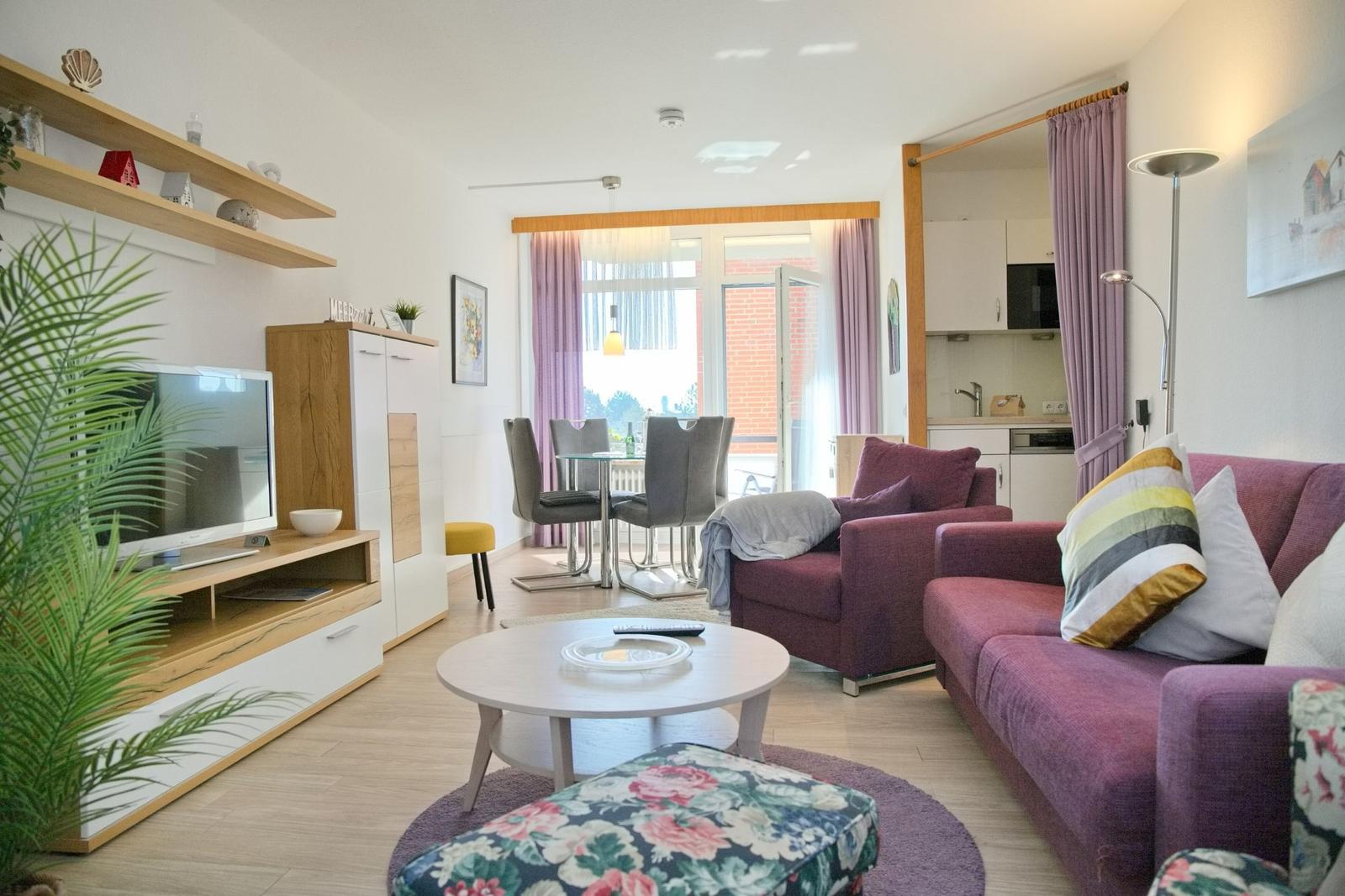 Wohnzimmer mit Sofa, Esstisch und TV-Möbel. Küche im Hintergrund.