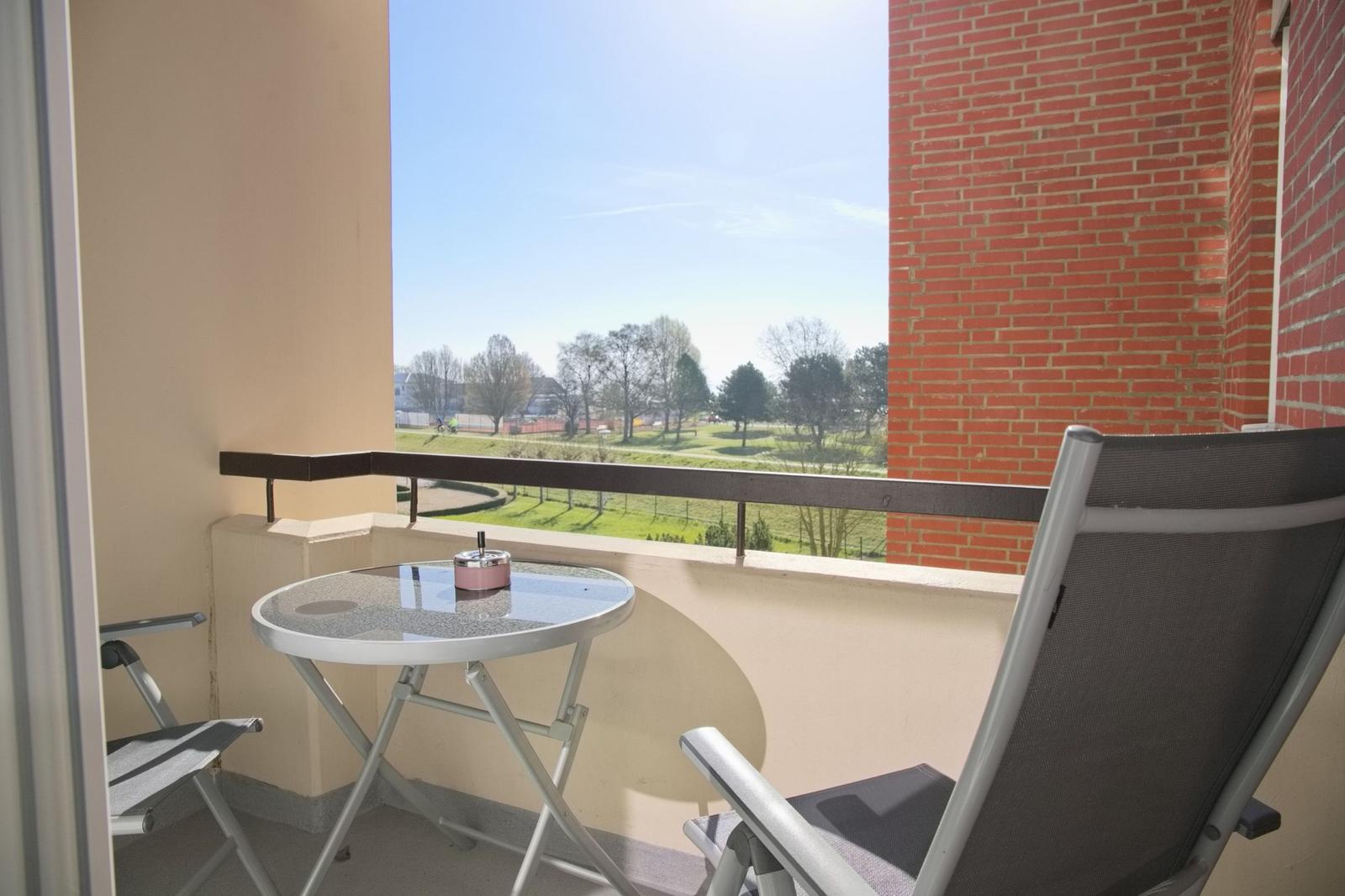 Balkon mit Tisch und Stühlen, Blick auf Grünfläche und Bäume.