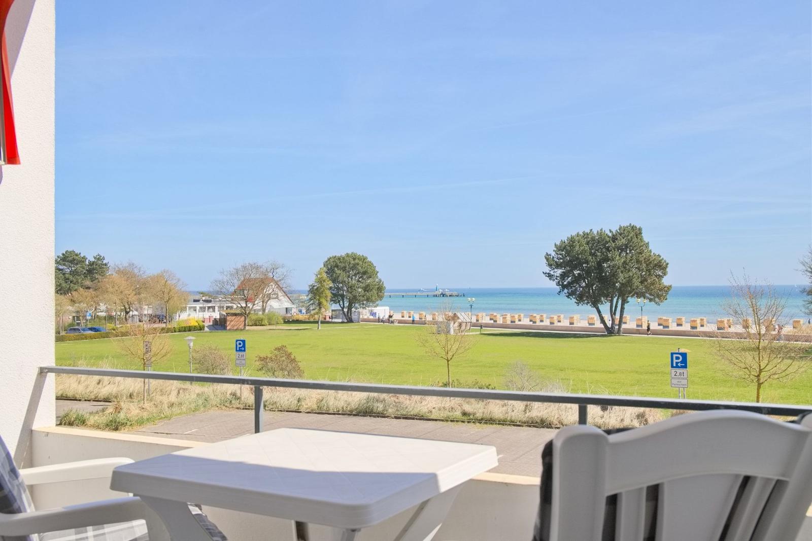 Terrasse mit Tisch und Stühlen bietet Blick auf Grünfläche und Meer.