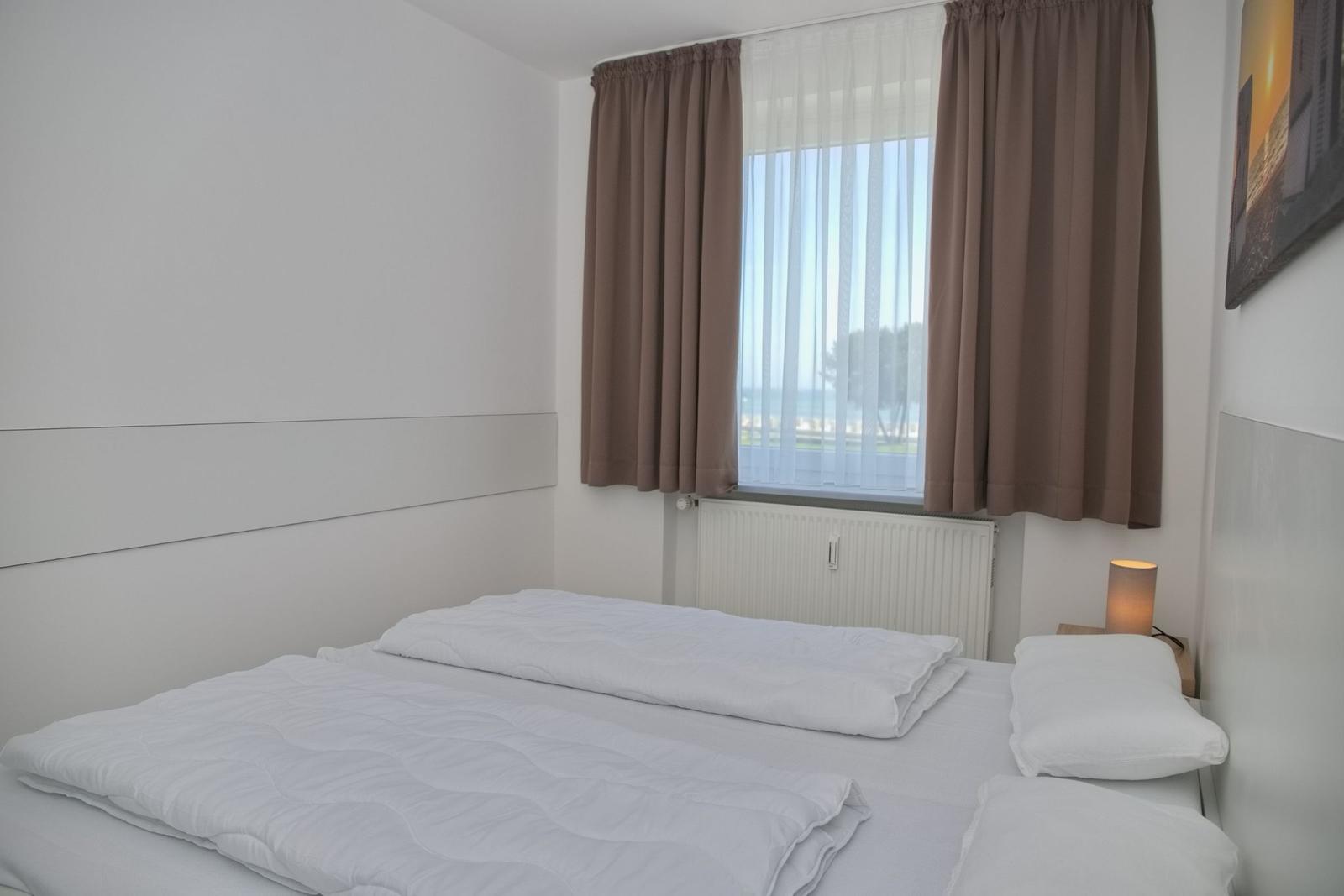 Schlafzimmer mit Bett, Fenster und Vorhängen.