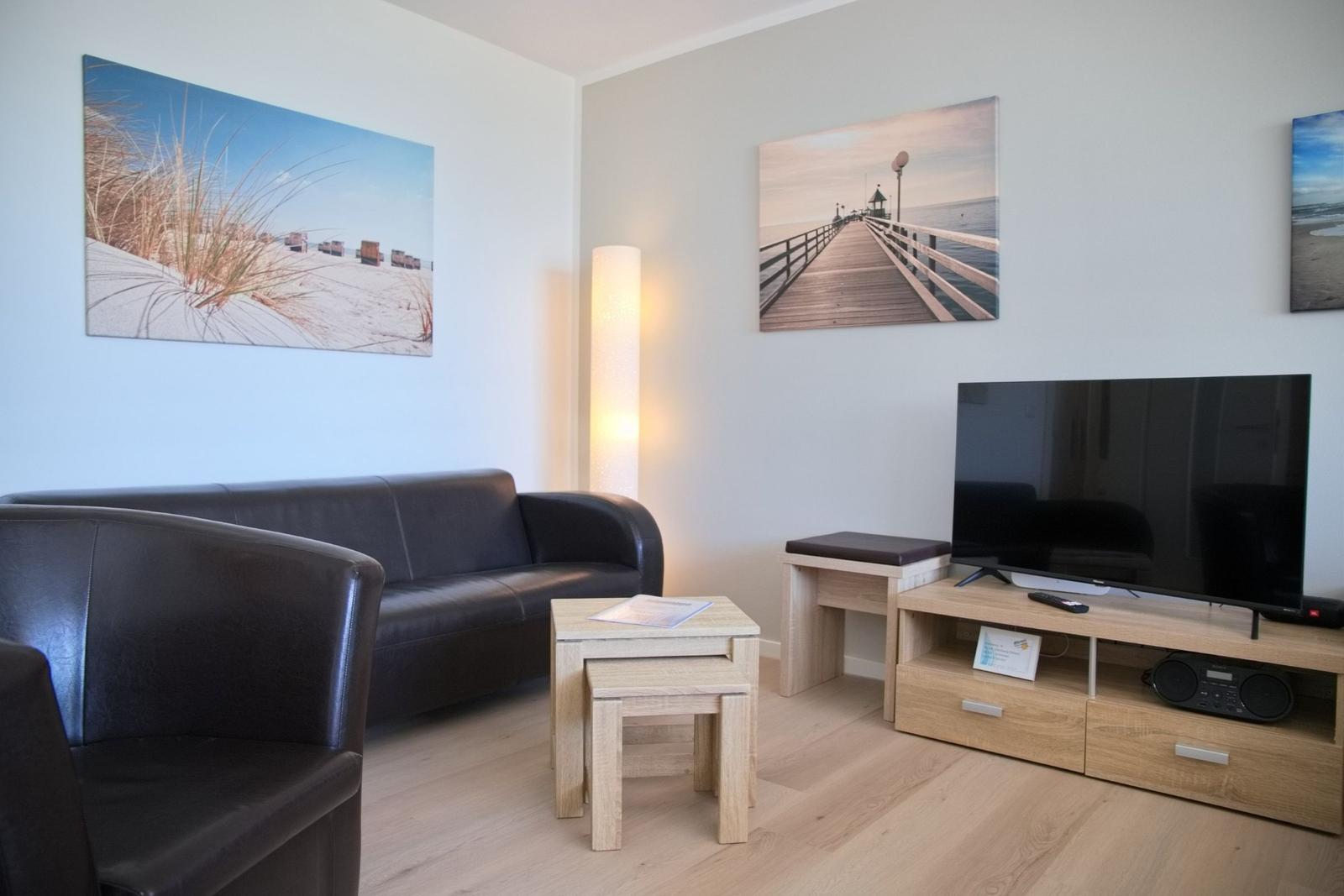 Wohnzimmer mit Sofa, Fernseher und Wandbildern an der Wand.