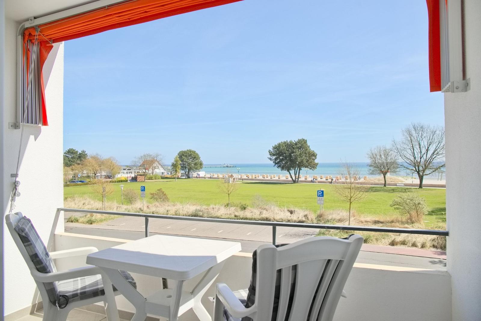Balkon mit Tisch und Stühlen, Blick auf Grünfläche und Strand.