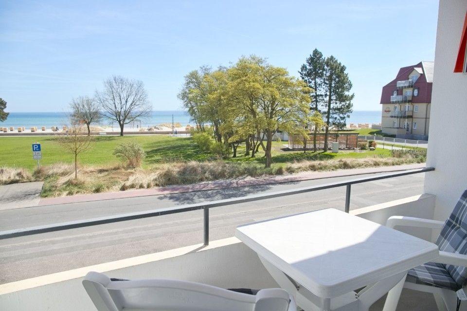 Terrasse mit Tisch und Stühlen, Blick auf Strand, Grünfläche und Hotel.