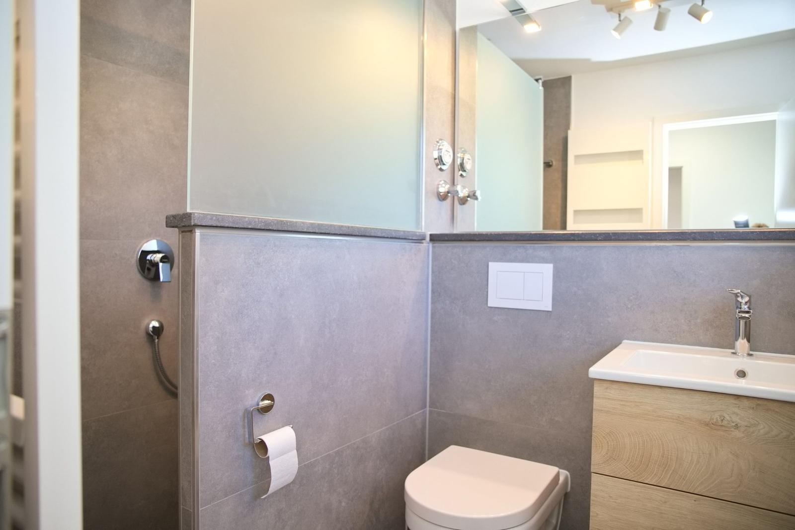 Badezimmer mit Dusche, Toilette und Waschbecken mit Spiegelschrank.
