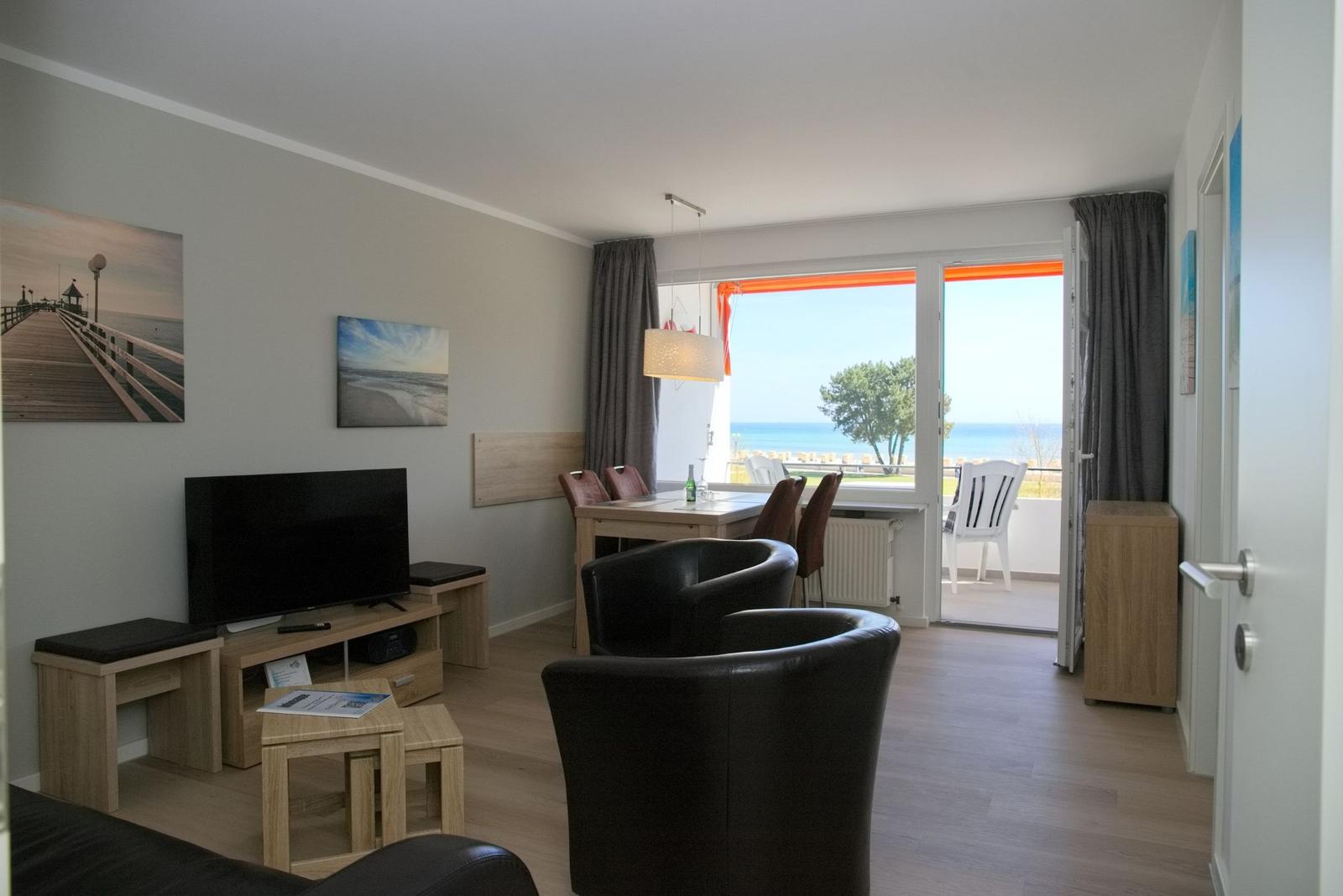 Wohn- und Essbereich mit Meerblick. Fernseher, Sessel und Tisch mit Stühlen.