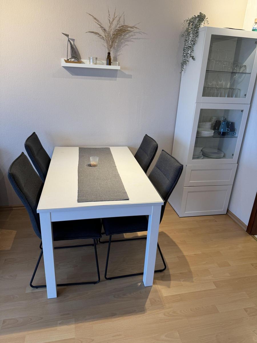 Esstisch mit vier Stühlen, Glasvitrine und Wandregal mit Dekoration.
