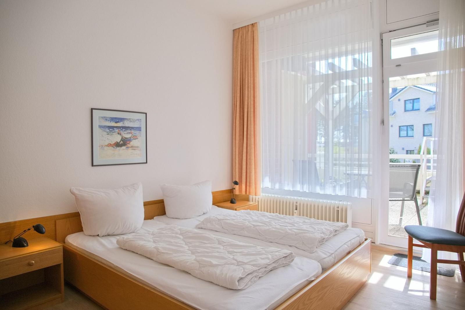 Zimmer mit Doppelbett, Fenster und Balkonansicht. An der Wand hängt ein Bild.