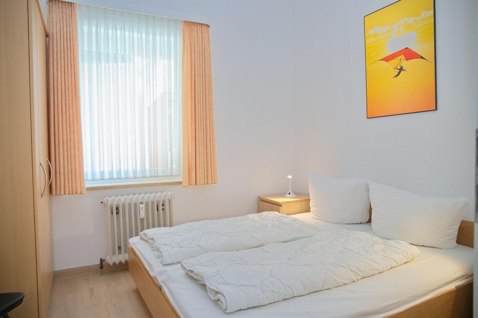 Schlafzimmer mit Bett, Nachttisch, Fenster und Wandbild.