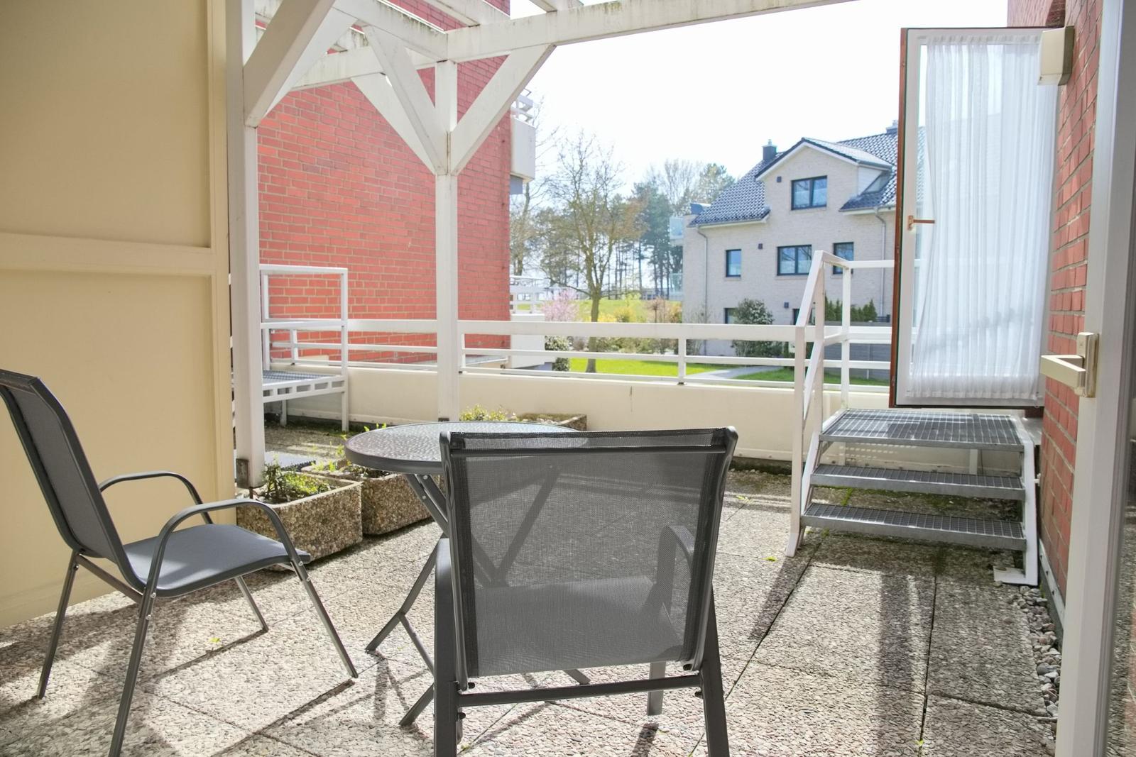 Terrasse mit Tisch und zwei Stühlen, Blick auf Wohnhaus und Grünfläche.