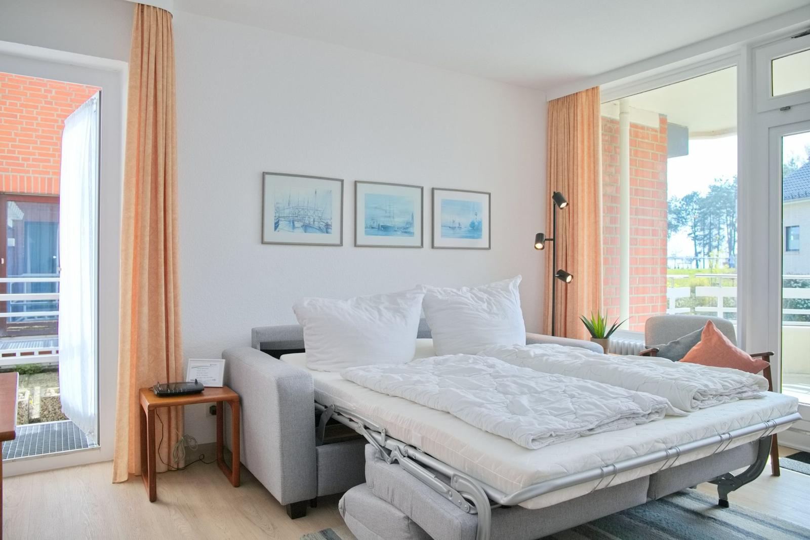 Schlafzimmer mit Schlafcouch, Fenstern und Bildern an der Wand.