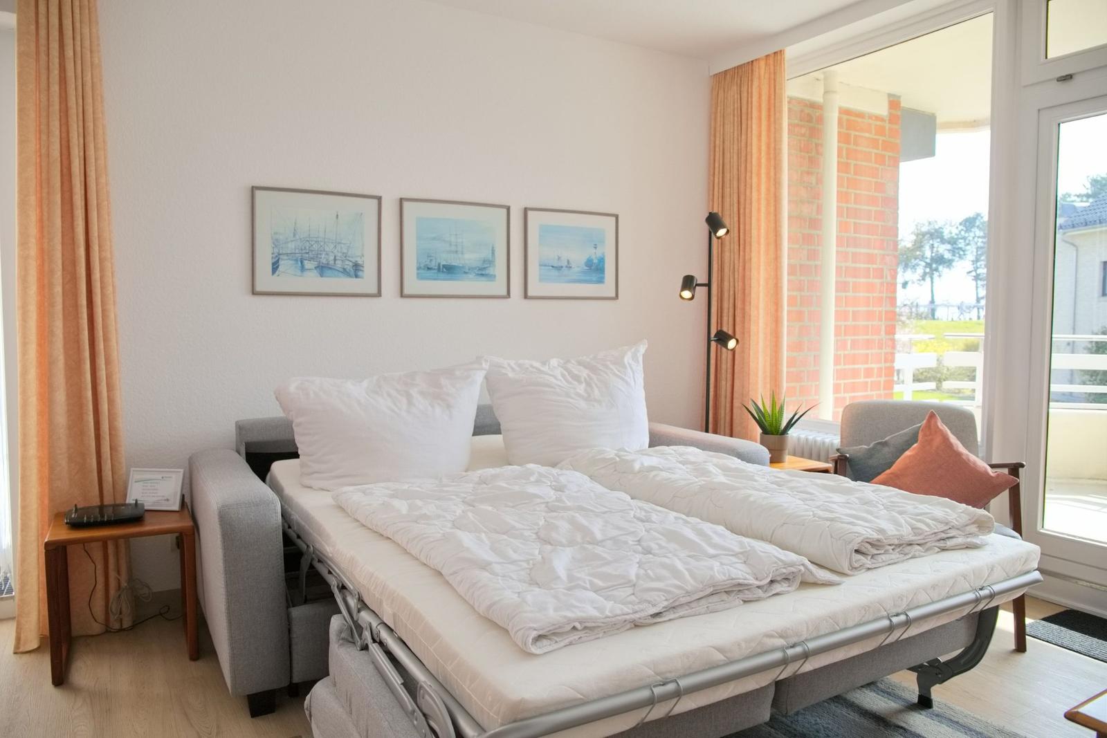 Schlafzimmer mit Schlafcouch, drei Bildern an der Wand und Blick auf Balkon.