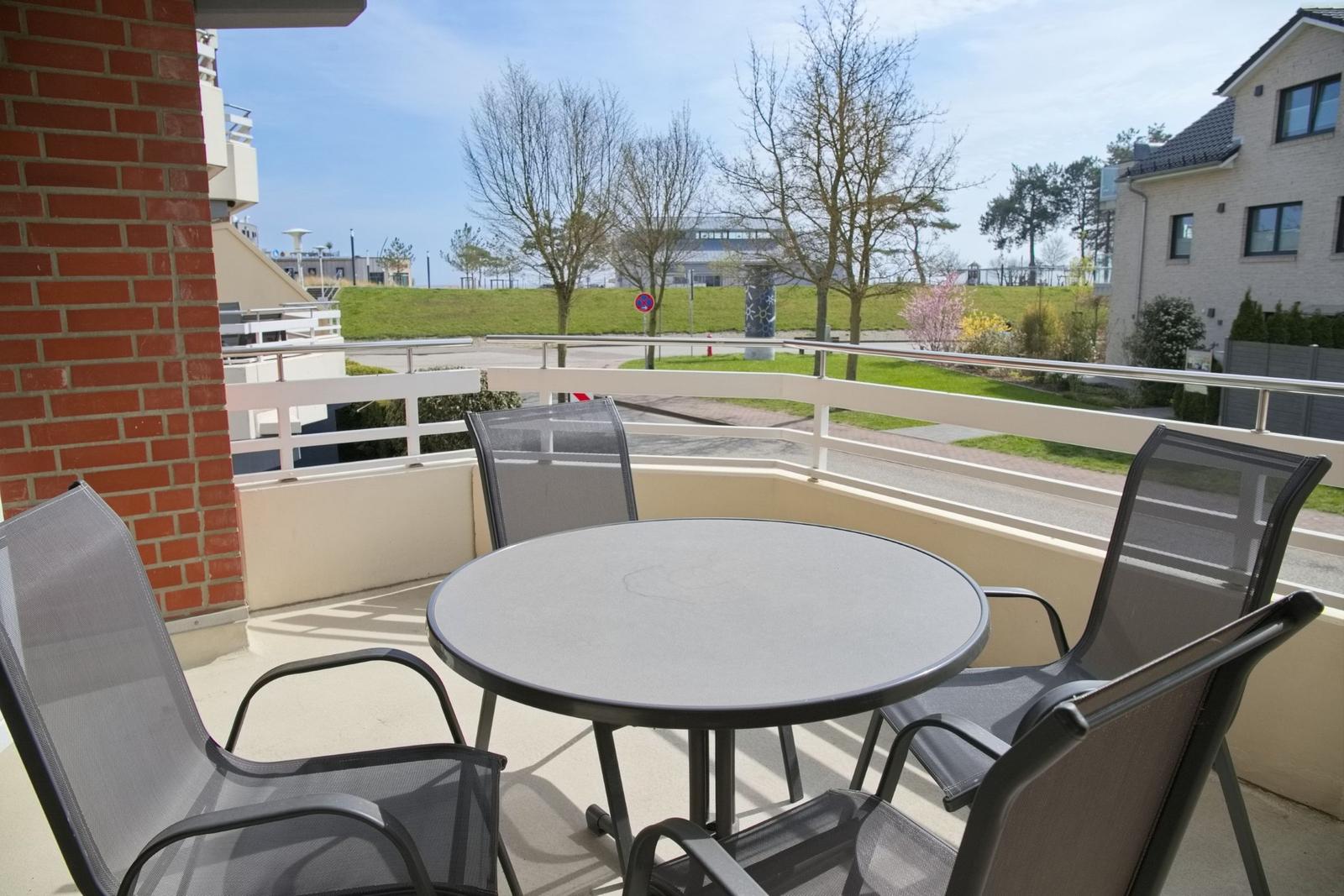 Terrasse mit runden Tisch und vier Stühlen. Blick auf Grünfläche und Gebäude.