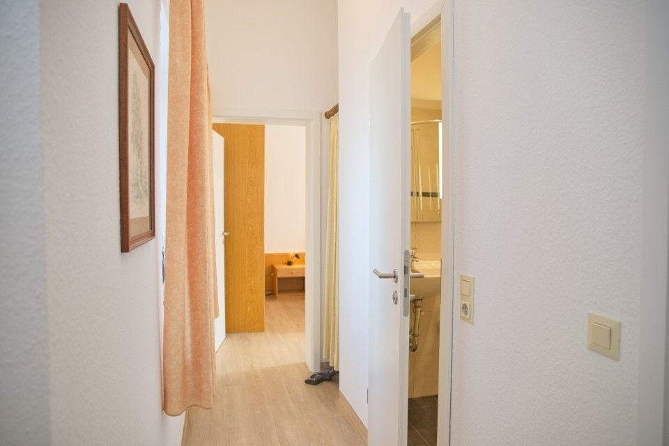 Flur mit Tür zu Bad und Blick in Schlafzimmer mit Holztür.