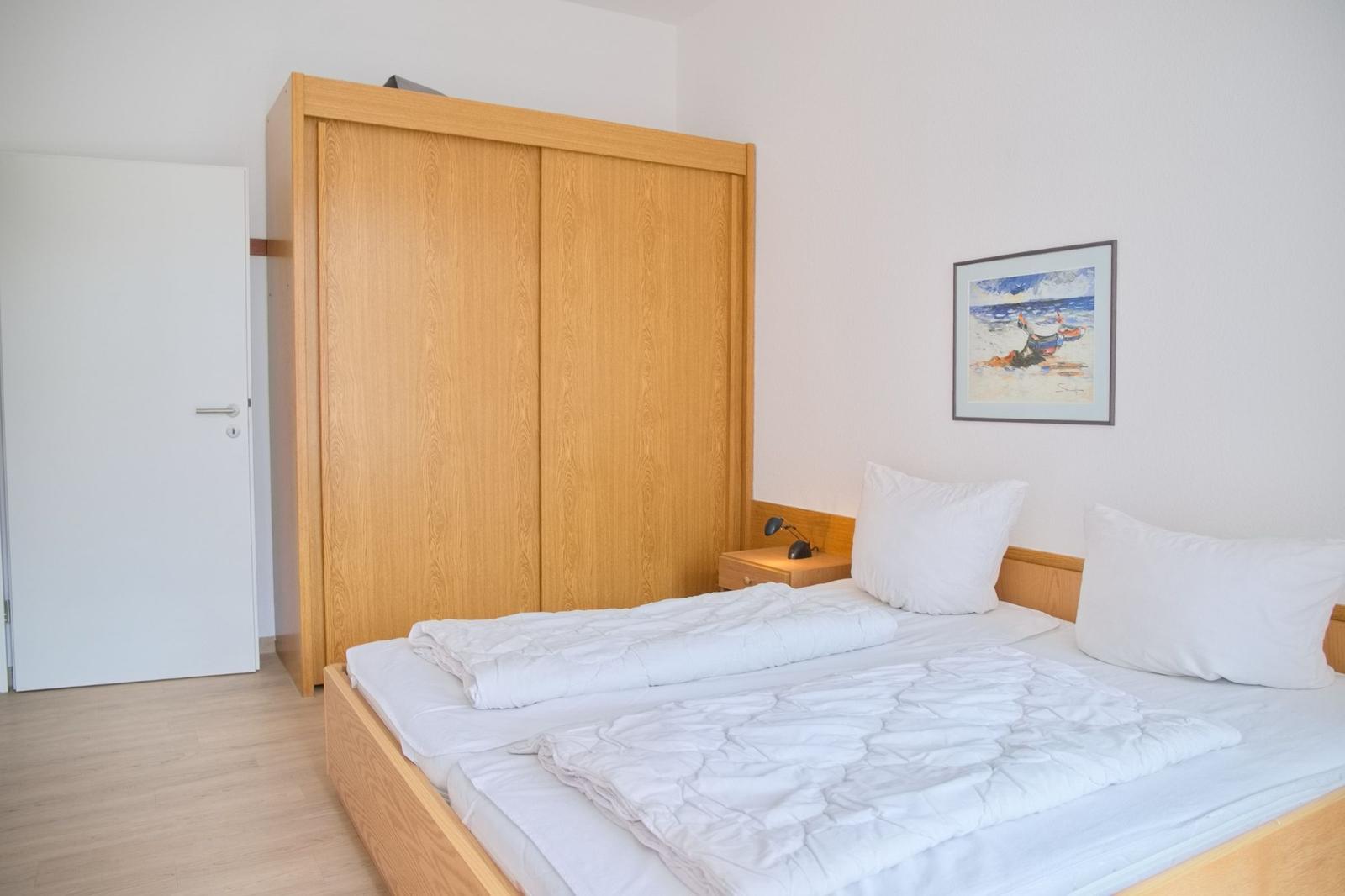 Schlafzimmer mit Doppelbett, Holzschrank und Wandbild.