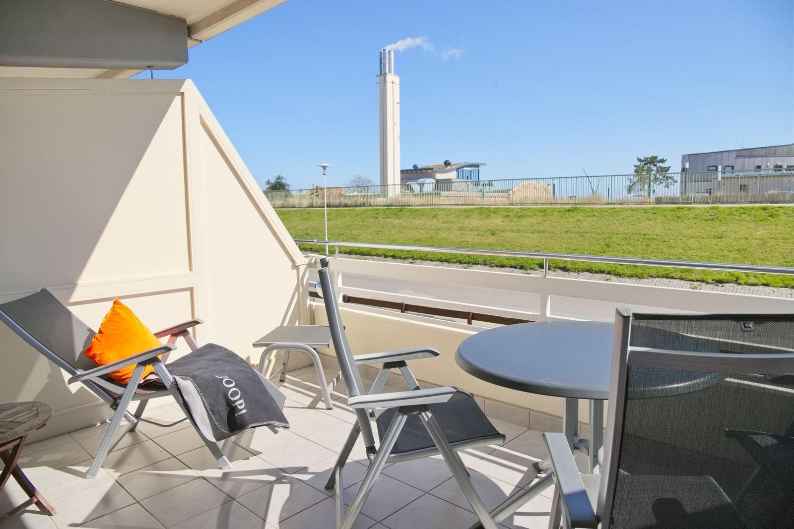 Terrasse mit Tisch, Stühlen und Blick auf Grünfläche und Industriegebäude.