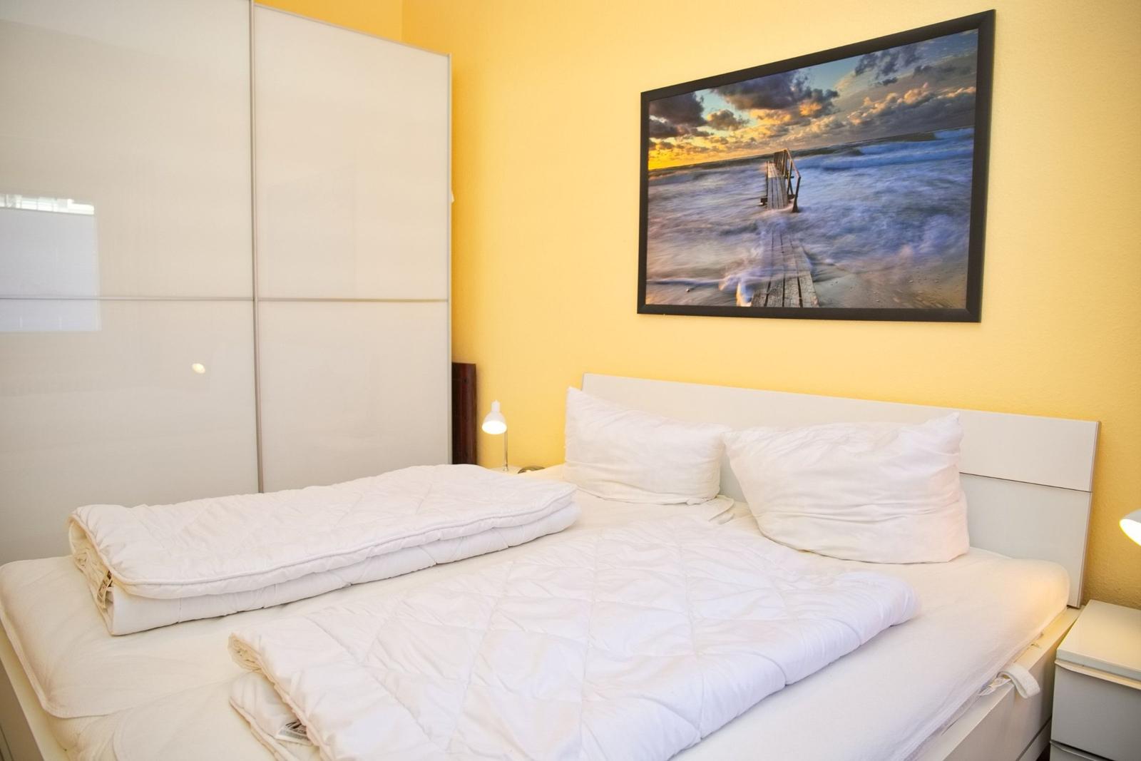 Schlafzimmer mit weißem Bett, Kleiderschrank und Wandbild
