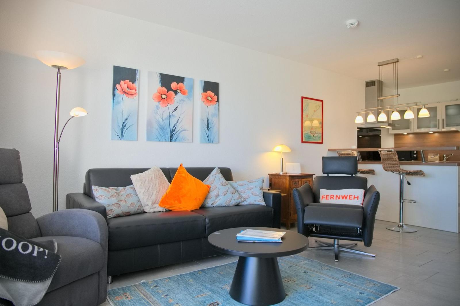 Wohnzimmer mit Sofa, Sesseln und Küchenbereich im Hintergrund.