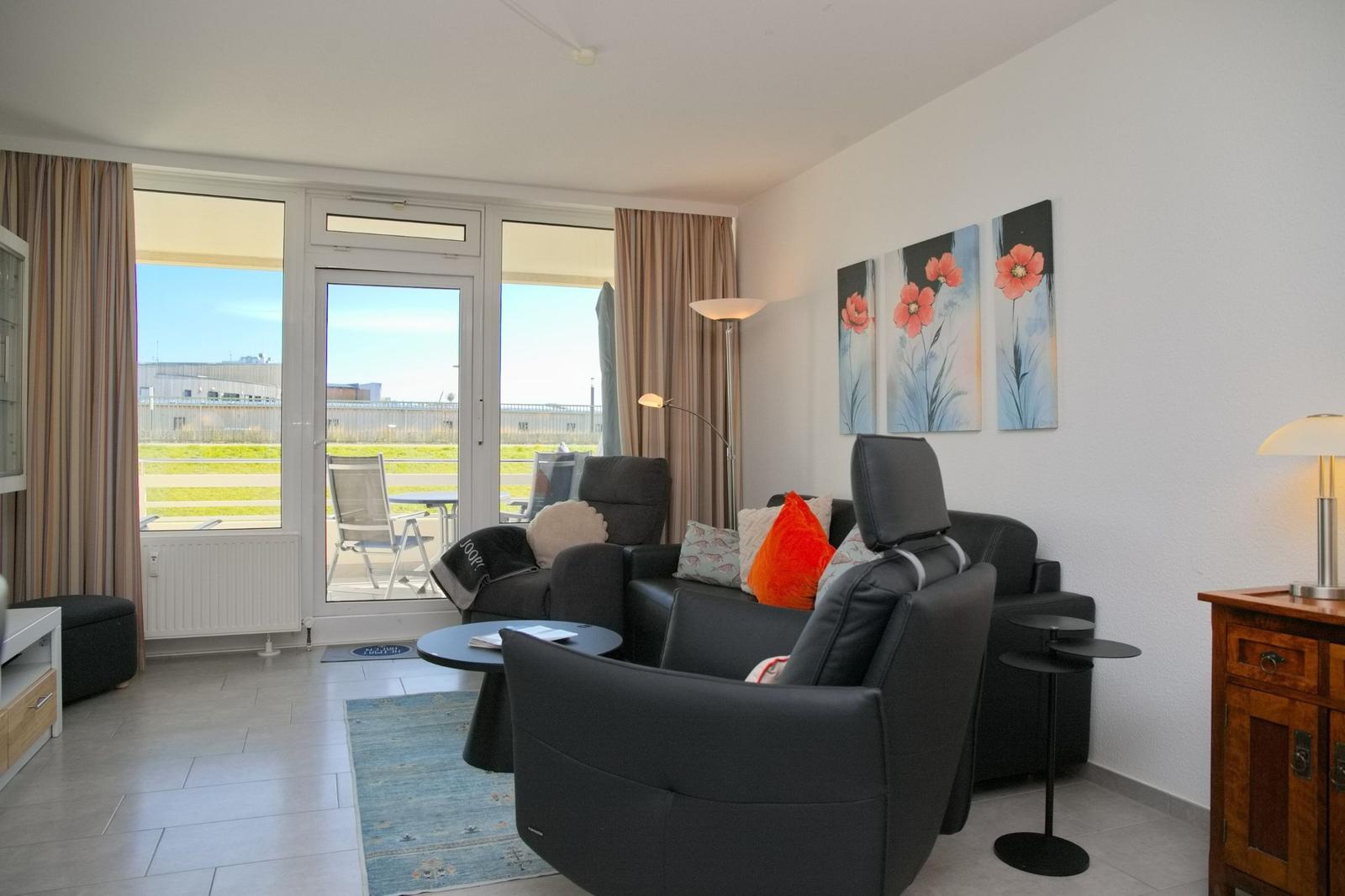 Wohnzimmer mit schwarzen Sesseln, Blumenbildern und Blick auf Terrasse.