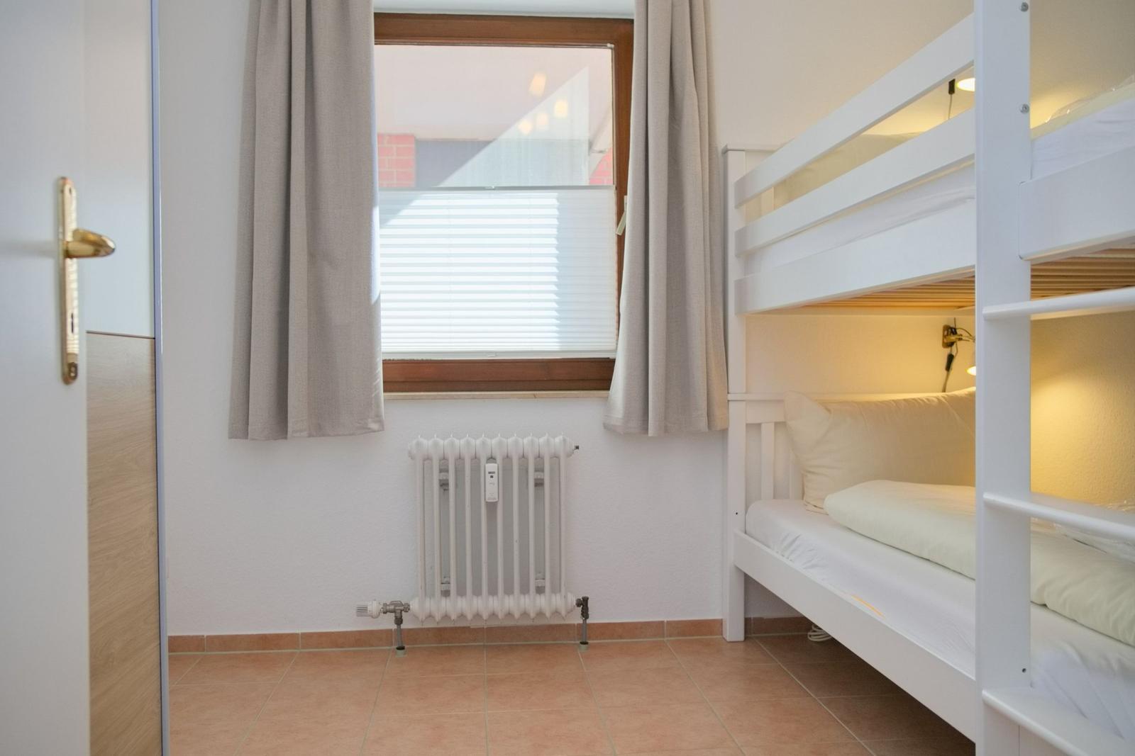 Zimmer mit Doppelstockbett, Fenster mit Jalousie und Heizkörper.