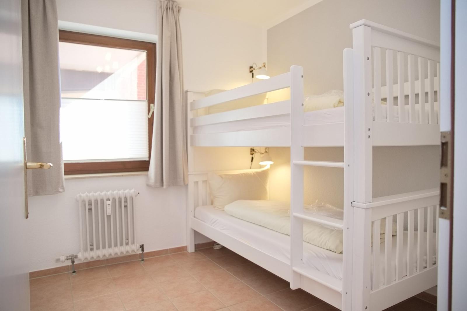 Zimmer mit weißem Doppelstockbett, Fenster und Heizkörper.