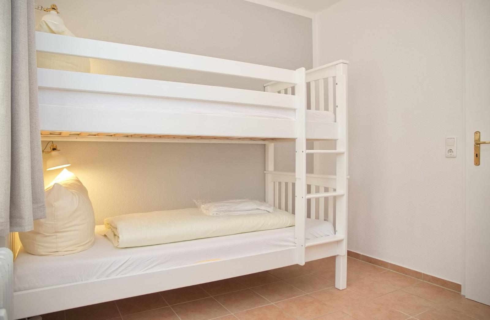 Zimmer mit weißen Doppelstockbetten, Beleuchtung und Tür