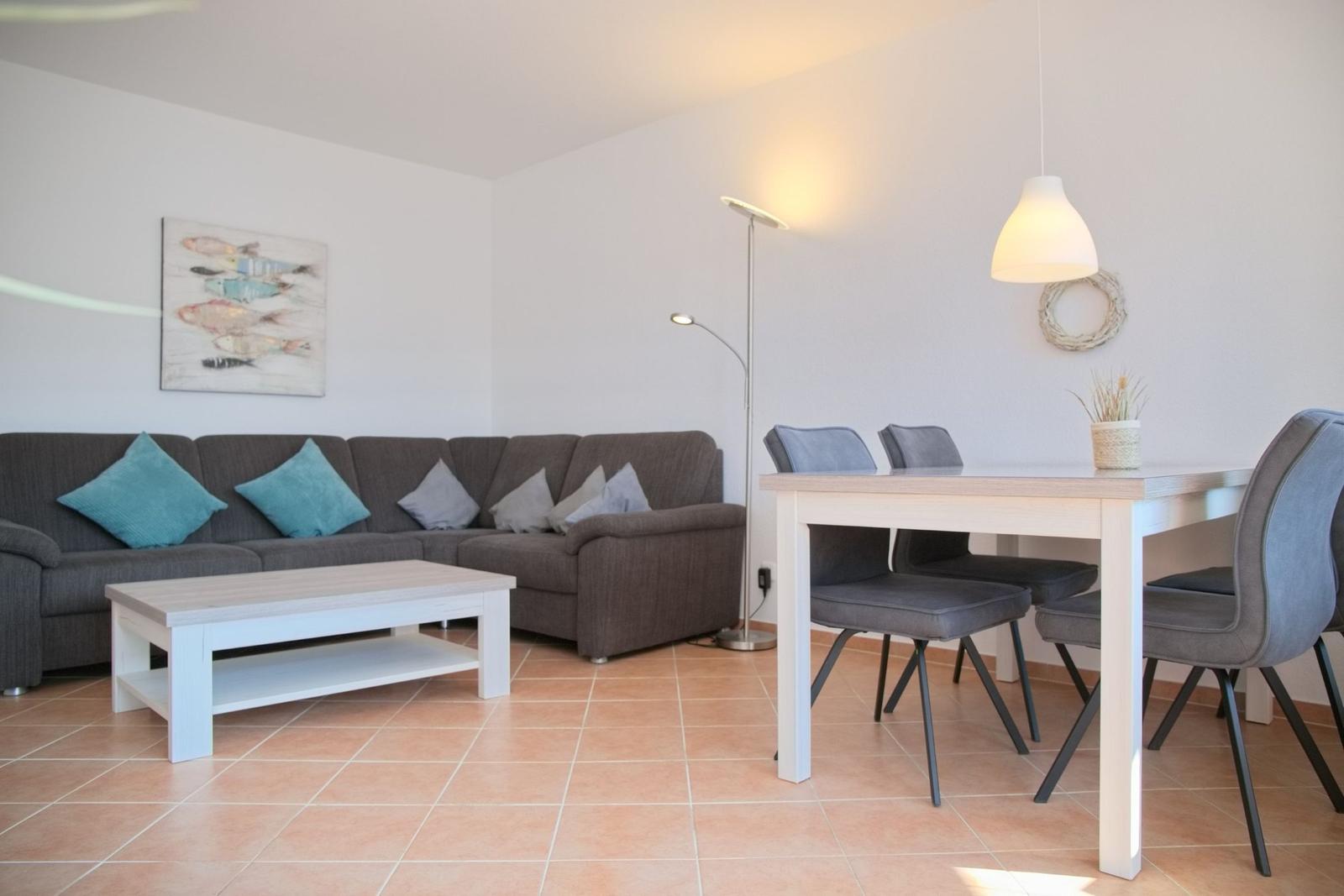 Wohn- und Essbereich mit Sofa, Tisch und Stühlen. Wandbild und Beleuchtung sichtbar.