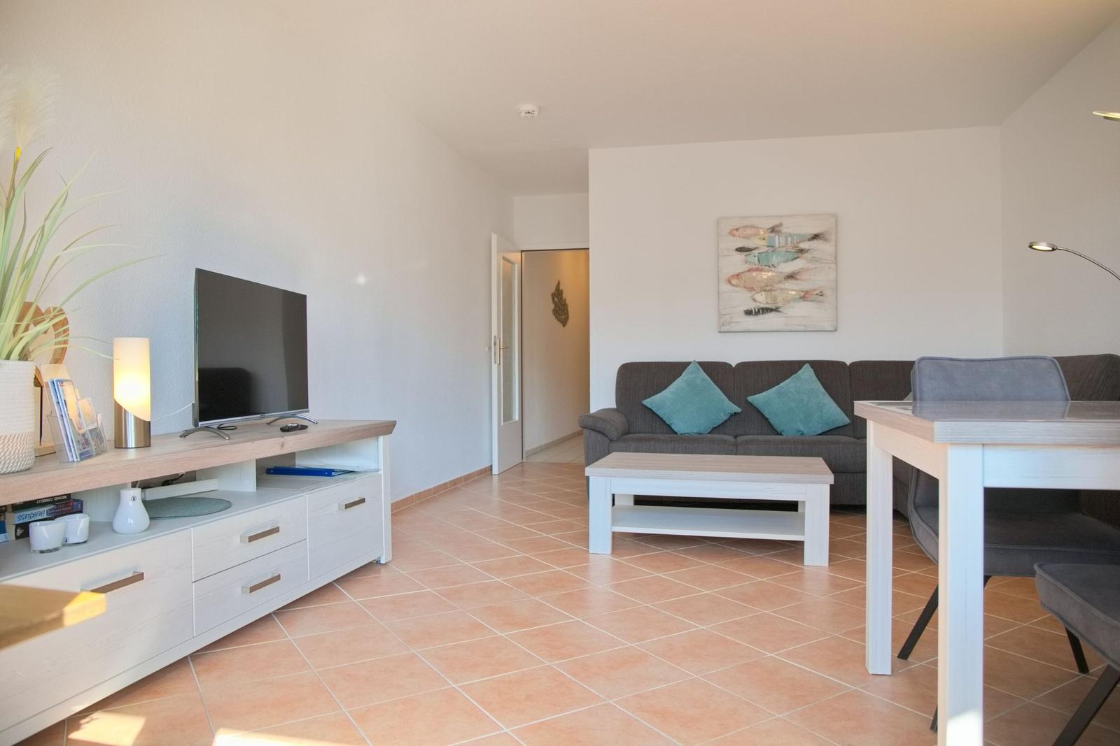 Wohn- und Essbereich mit Sofa, TV und Esstisch. Teppichboden und Wandbild.
