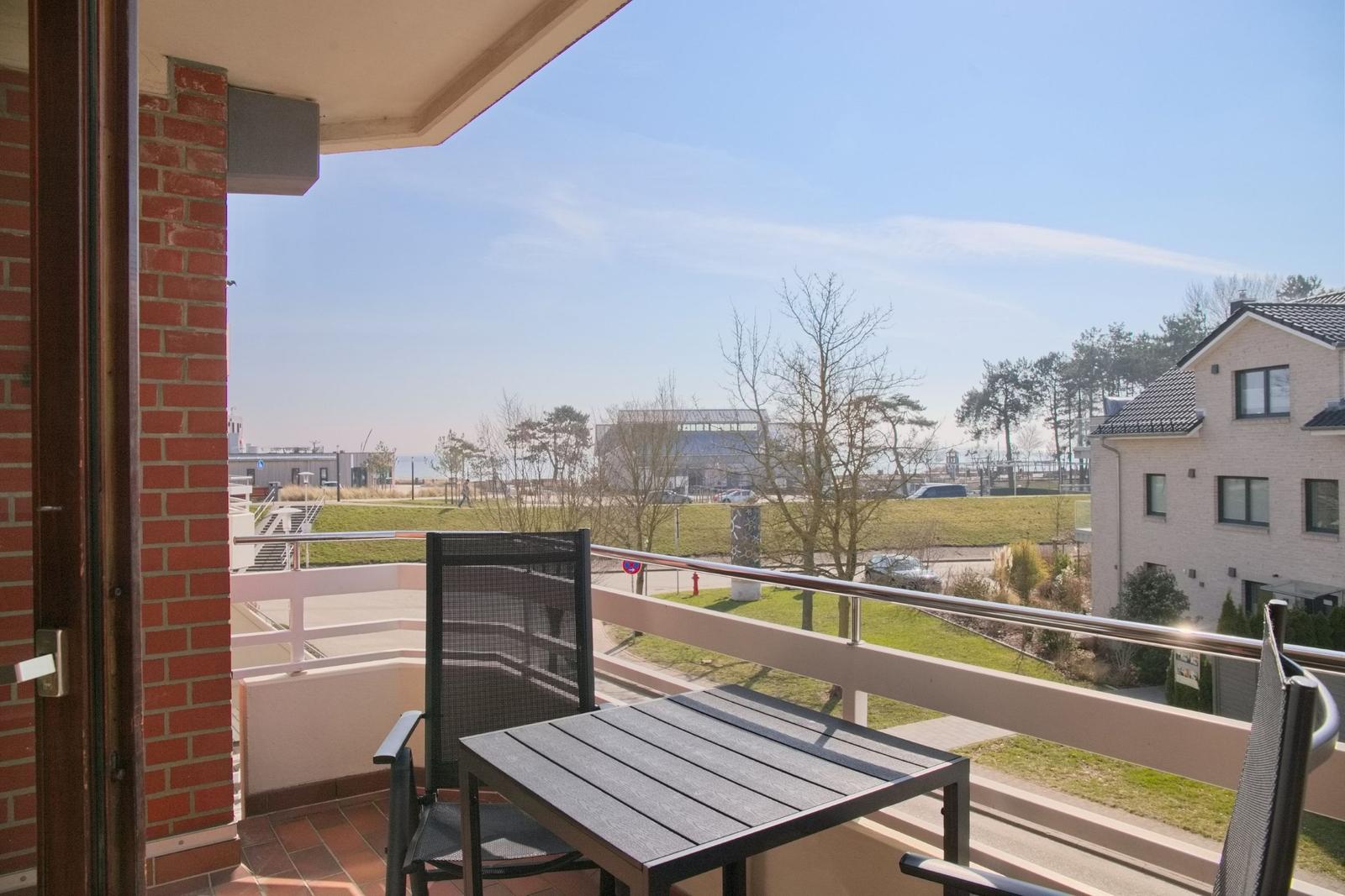 Balkon mit Tisch und Stühlen, Blick auf Grünfläche und Gebäude.